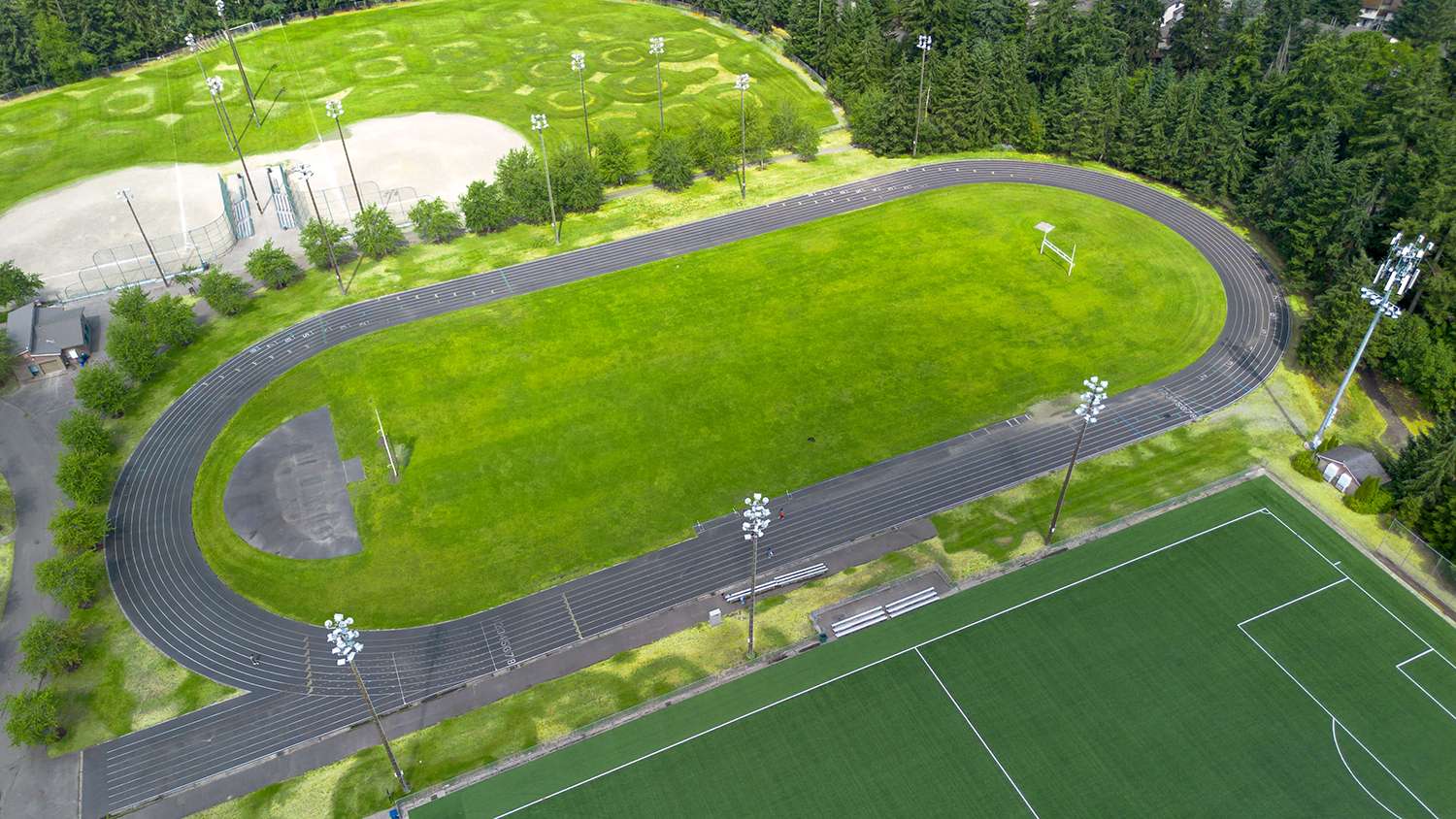 Aerial view of a Saghalie Park running track surrounded by dense trees. Additional baseball diamonds are visible beyond the track.